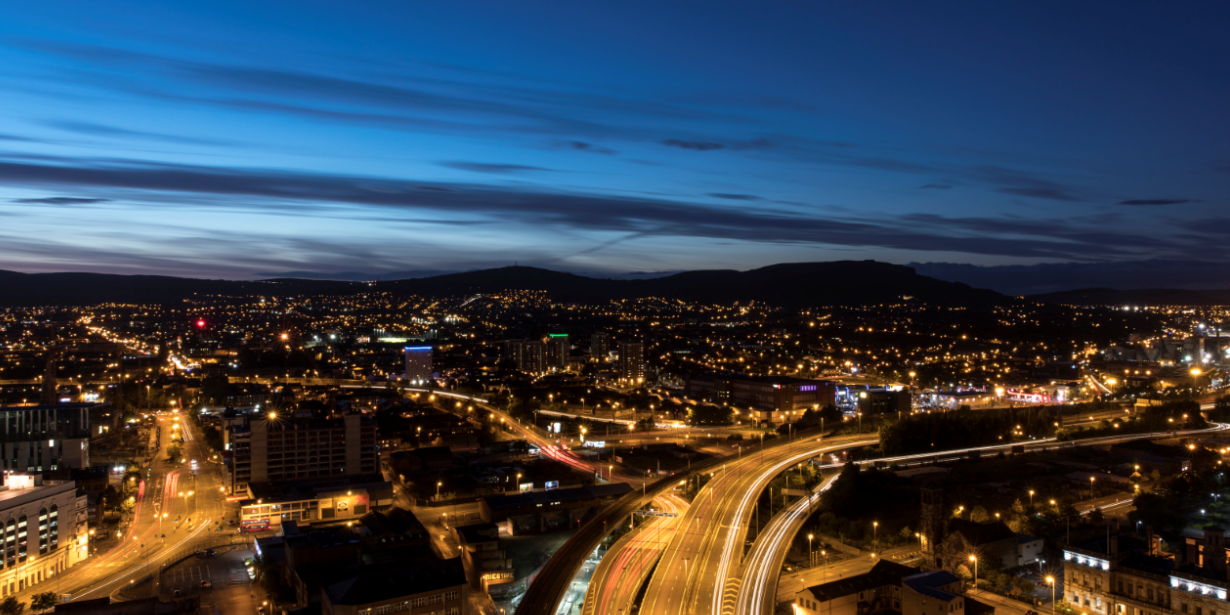 Night time cityscape of Belfast showing roads and motorways, street lights and mountains in the distance