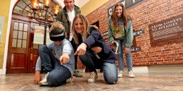 A family using virtual reality headsets and pointing at a map of Belfast on the ground in Belfast City Hall